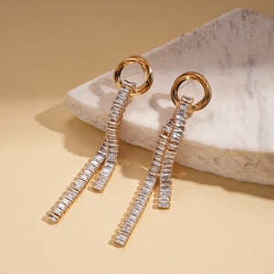 Detailed view of gold tassel earrings with rectangular zircons on textured stone