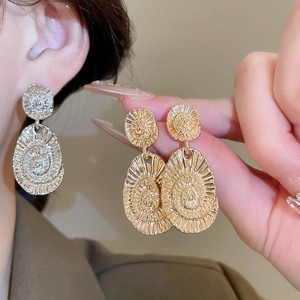 Macro detail of oval swirl texture on vintage metallic drop earrings with gold finish