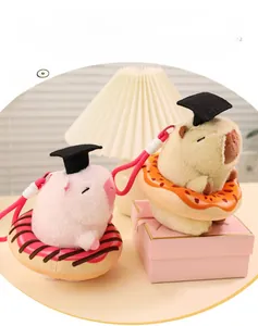 Close-up of pink and beige capybara plush keychains wearing academic caps on donuts