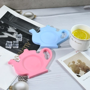 Pink and blue teapot shaped silicone coasters on a white wooden surface in a cozy kitchen setting