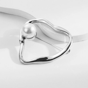 Detail of silver heart brooch with pearl inlay on a minimalist textured surface