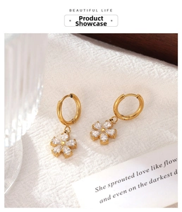 Detailed view of golden flower earrings with zircon petals on white textured fabric