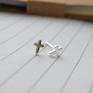 Macro close-up of minimalist 925 silver cross stud earrings on a clean lined paper background