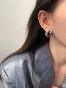 Close-up of a silver sunflower petal earring worn with a stylish blue blazer