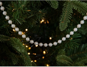 White pearl bead chain garland draped on a Christmas tree with warm ambient lighting