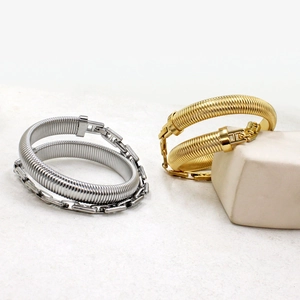 Close-up of gold and silver Tubogas spring bracelets with chain clasp on a textured surface