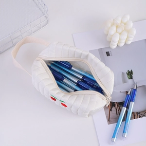 Draufsicht auf ein weißes gestepptes Etui mit Kirschstickerei und blauen Gelschreibern