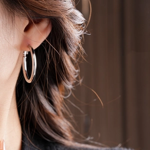 Close-up of a silver hoop earring worn by a model, showing sleek minimalist jewelry design