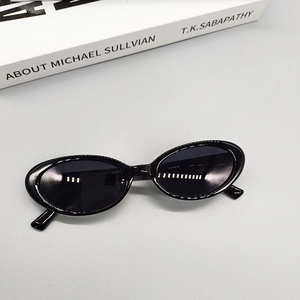Detail of vintage black oval sunglasses on a grey surface with artistic book props