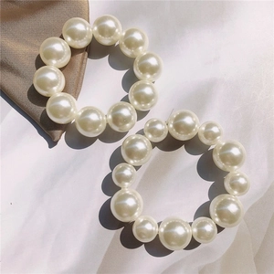Elegant set of two large lustrous pearl hair ties on silk and white fabric background