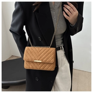 Brown suede crossbody bag with V-quilted texture and gold chain strap on a model