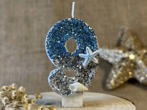 Macro view of blue glitter number 9 birthday candle with starfish on wooden base