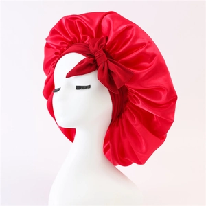 Red satin sleep bonnet for hair care featuring a large decorative silk-like bow on white base