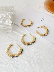 Detailed shot of hexagonal earrings with colorful zircon inlays on white textured backdrop