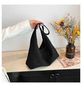 Minimalist black tote bag in matte fabric held by a person in a white blazer