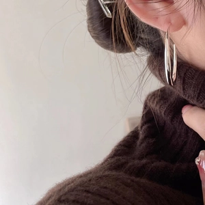 Close-up of minimalist large silver hoop earrings worn with a cozy brown sweater