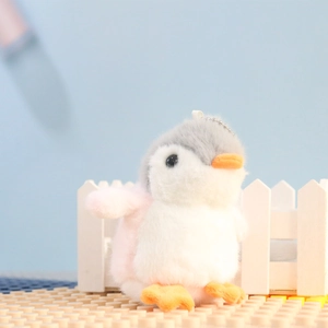 Close-up of a cute plush penguin keychain with grey fur and pink cheeks on a white fence