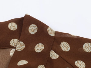 Gros plan du col d'un chemisier en mousseline marron à pois avec détails de couture fins