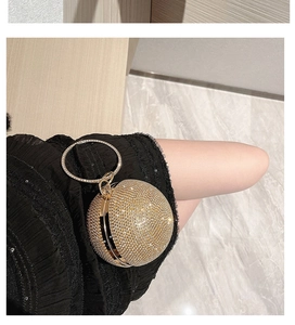 Close-up of a golden spherical rhinestone evening bag with a metal ring handle shown in hand