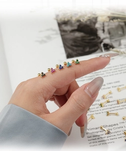 Macro shot of five colors of mini flower stud earrings held on a finger for size reference