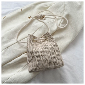 Detail of woven straw bucket bag with drawstring closure and golden metal eyelets