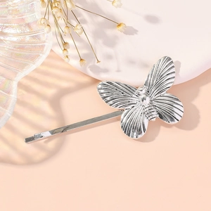 Silver butterfly metal hair clip with textured details on a soft pink background