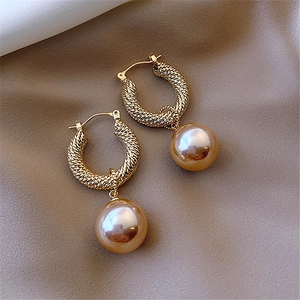 Detailed macro view of champagne pearl earrings with gold twisted metal rings on silk