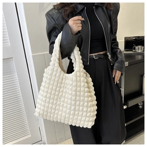 Détail d'un sac crème à texture gaufrée porté par un mannequin au style moderne