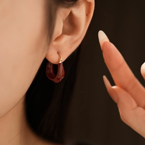 Close-up of deep red U-shaped resin hoop earrings with gold-plated clasp on ear