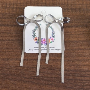 Macro shot of silver bow earrings with long snake chain tassels on a display card