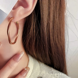 Close-up of golden twisted hoop earrings with metallic finish worn by a model