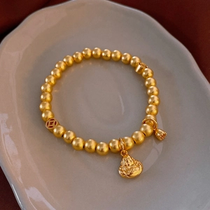 Detailed macro shot of a golden bead bracelet with lucky charms on a gray ceramic plate