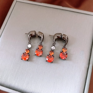 Macro detail of drop earrings with orange gems and dark metal hooks on gift box