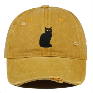 Close-up of black cat embroidery and distressed details on a mustard yellow cotton cap