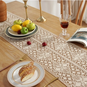 Beige lace crochet table runner with tassels on a wooden dining table in Nordic style
