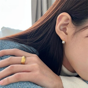 Detail of model wearing gold ripple ring and square crystal stud earring with tweed jacket