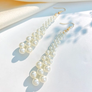 Elegant long tassel pearl earrings with gold hooks on white silk background