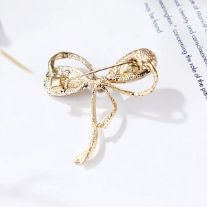 Macro view of gold bow brooch back showing alloy pin closure and textured frosted finish