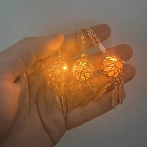 Gros plan de colliers pendentifs attrape-rêves lumineux avec plumes tenus en main
