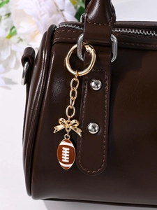 Close-up of brown leather handbag with a golden football charm and bowknot keychain