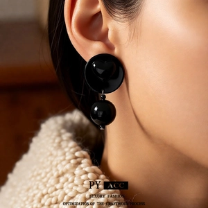 Chic black acrylic heart and ball drop earrings worn by a model in a professional close-up shot