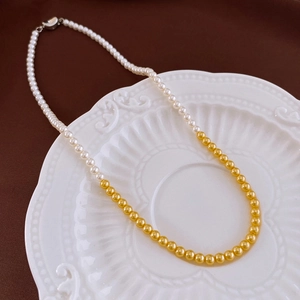 Detail of French vintage necklace with white pearls and gold beads on a white ceramic plate