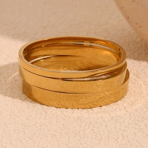 Minimalist stackable 18K gold plated stainless steel bangles set on stone background
