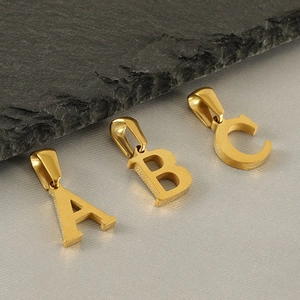 Macro detail of three golden alphabet pendants A, B, and C on a textured stone surface