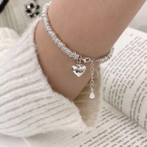 Chic multi-layered silver heart pendant bracelet on model with cozy knit sweater background