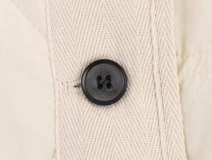 Macro detail of black four-hole button on beige herringbone texture jacket fabric