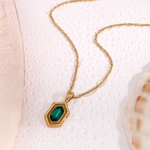 Detail view of 18K gold hexagon pendant with green stone on a water-beaded surface