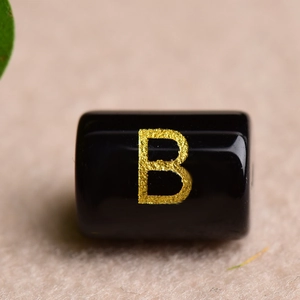 Macro detail of a black rectangular bead with a gold letter B for DIY jewelry making