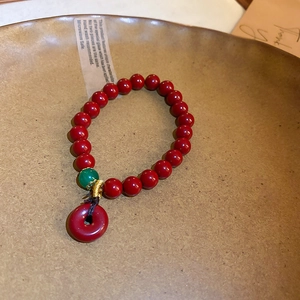 Détail du bracelet en perles d'agate rouge avec breloque beignet et finitions dorées