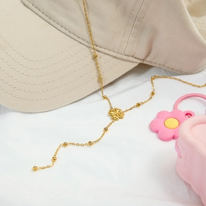 Détail du collier trèfle doré avec perles posé sur une casquette en arrière-plan